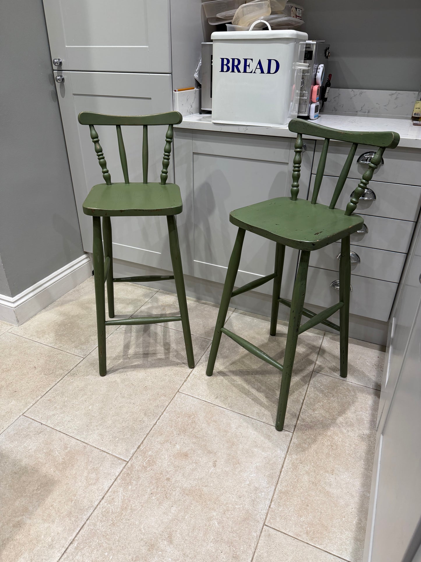 green stool chairs with back infant of grey kitchen with bread bin on counter top 
