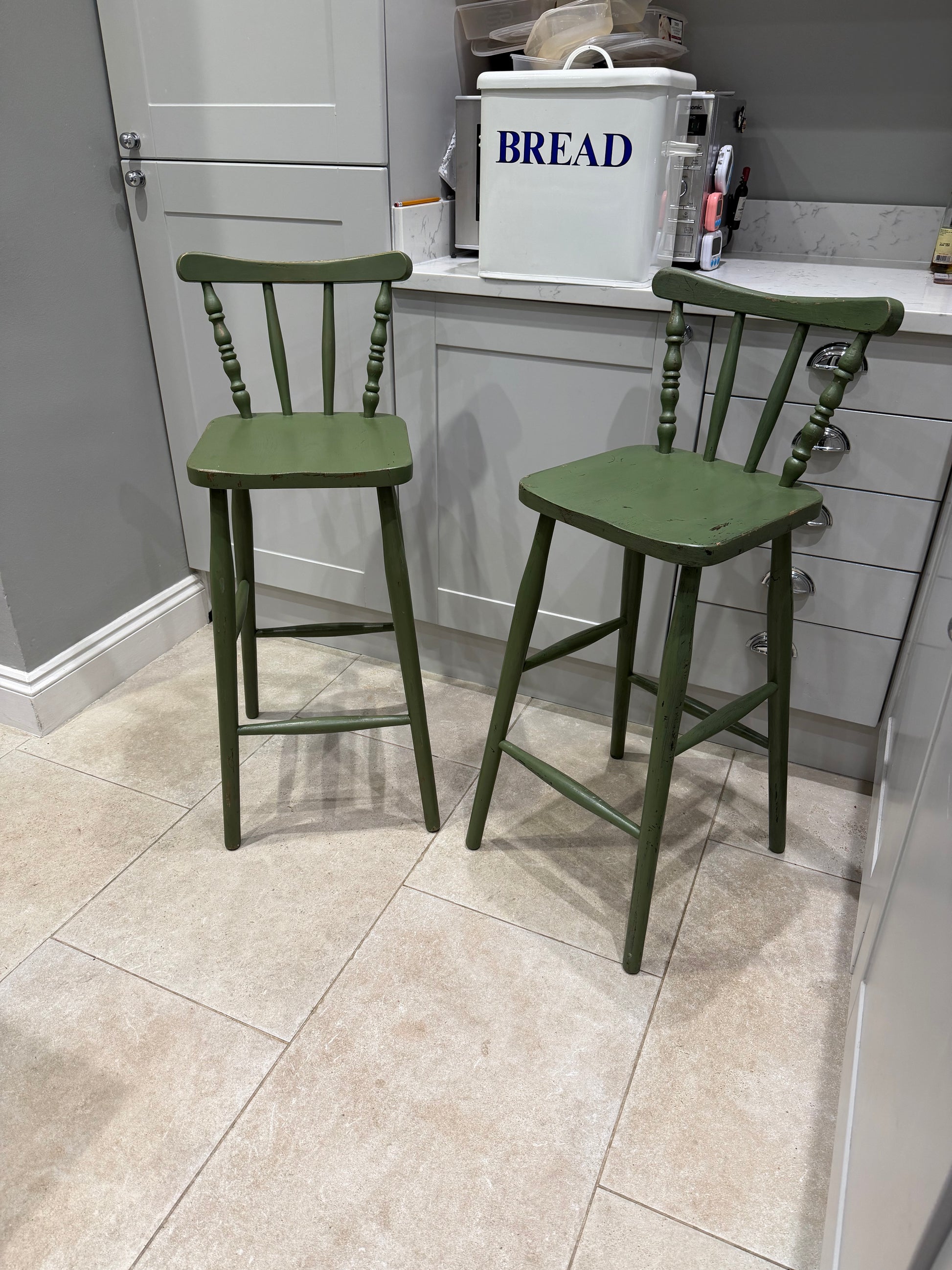 green stool chairs with back infant of grey kitchen with bread bin on counter top 
