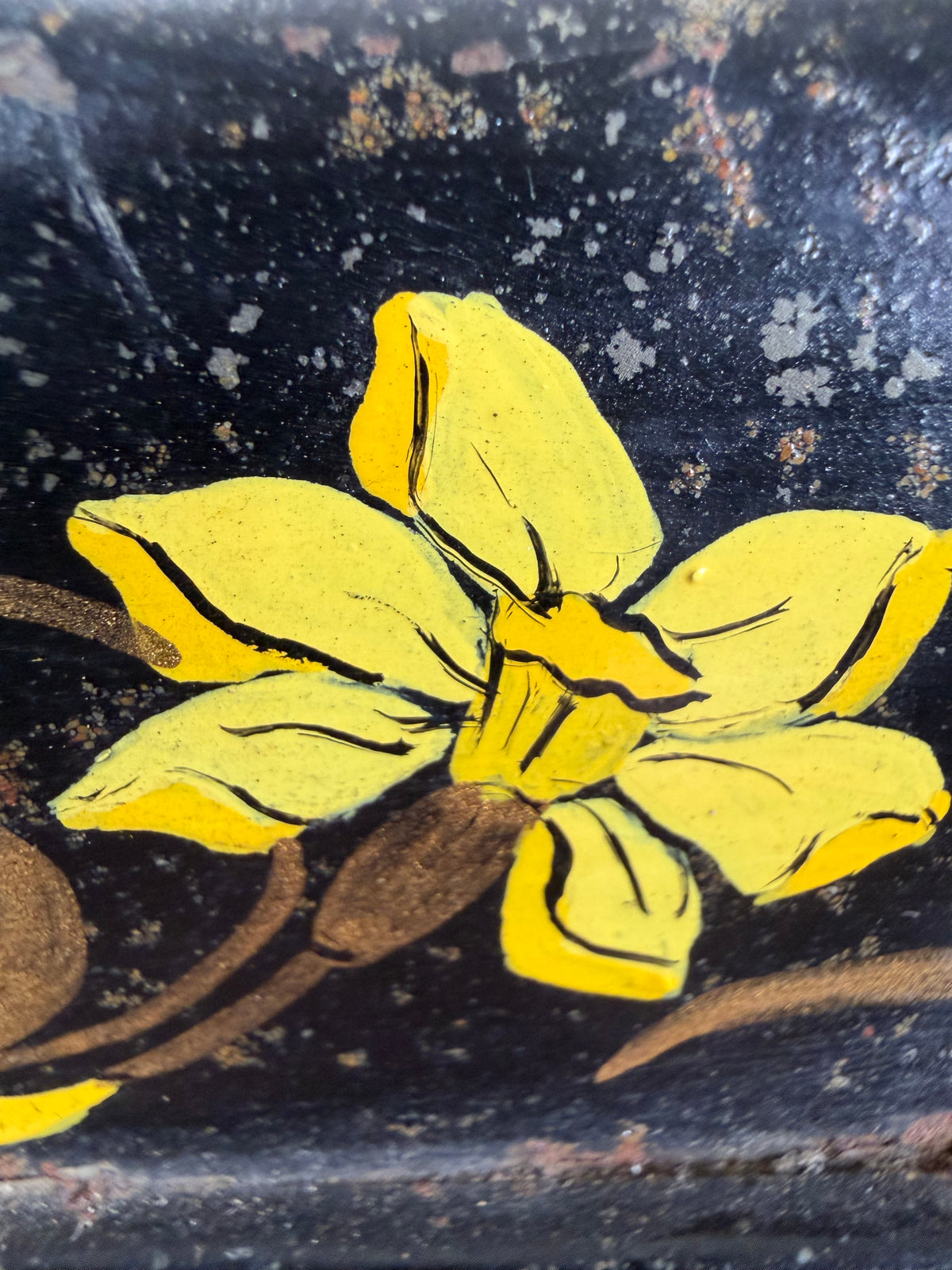 A close-up of a hand-painted yellow daffodil flower with black outlines on a dark, speckled black background.